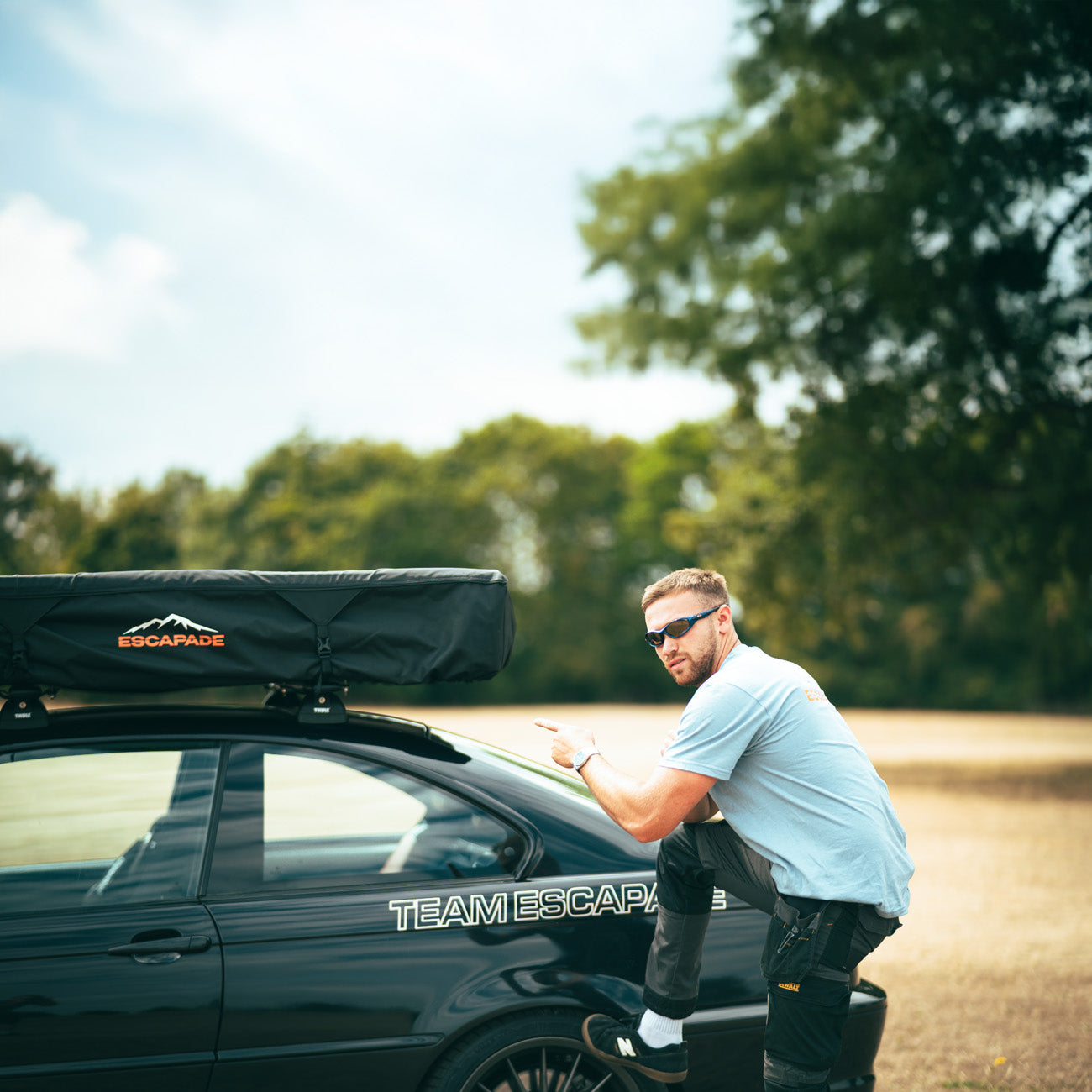 Man standing next to a car with a roof rack and 'Team Escapade' branding.